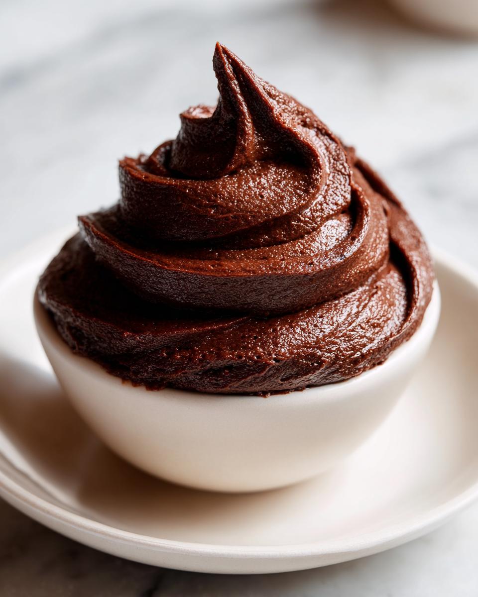 A perfect swirl of rich, dark chocolate frosting piped into a small white bowl.