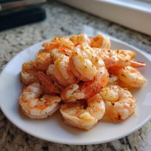 A pile of perfectly cooked, seasoned air fryer frozen shrimp served on a white plate.