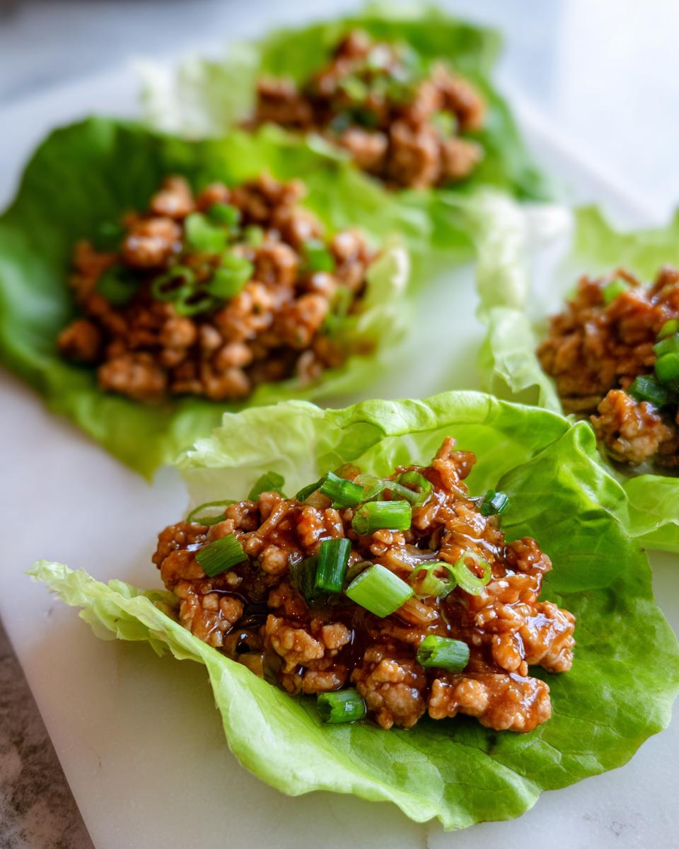 Close-up of savory ground chicken filling served in crisp lettuce cups for chicken lettuce wraps, topped with green onions.