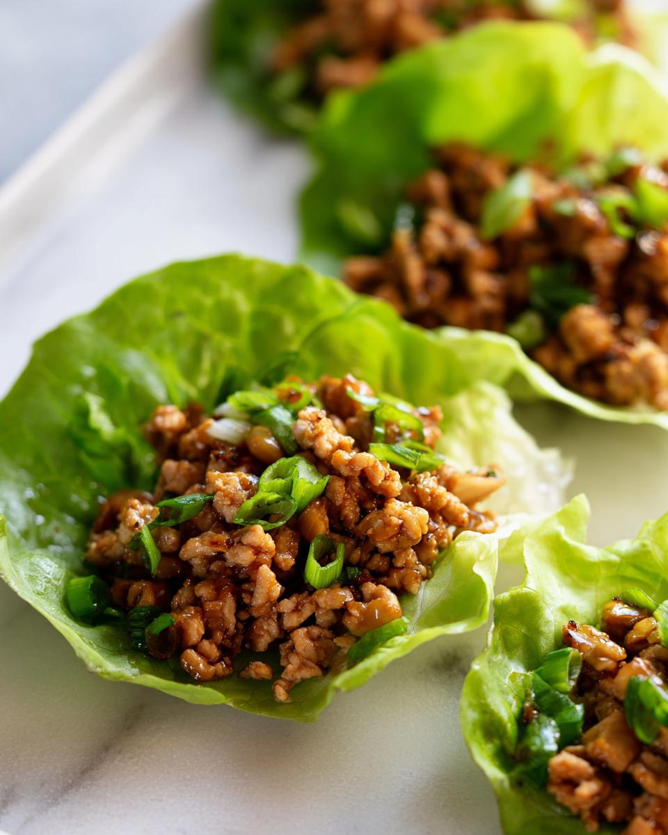 Close-up of savory ground chicken filling topped with green onions served in crisp lettuce cups for chicken lettuce wraps.