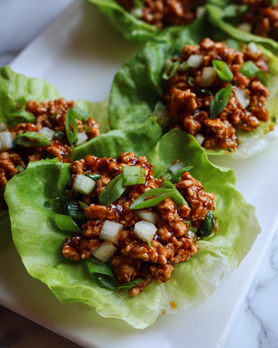 Close-up of three servings of flavorful chicken lettuce wraps topped with green onions.
