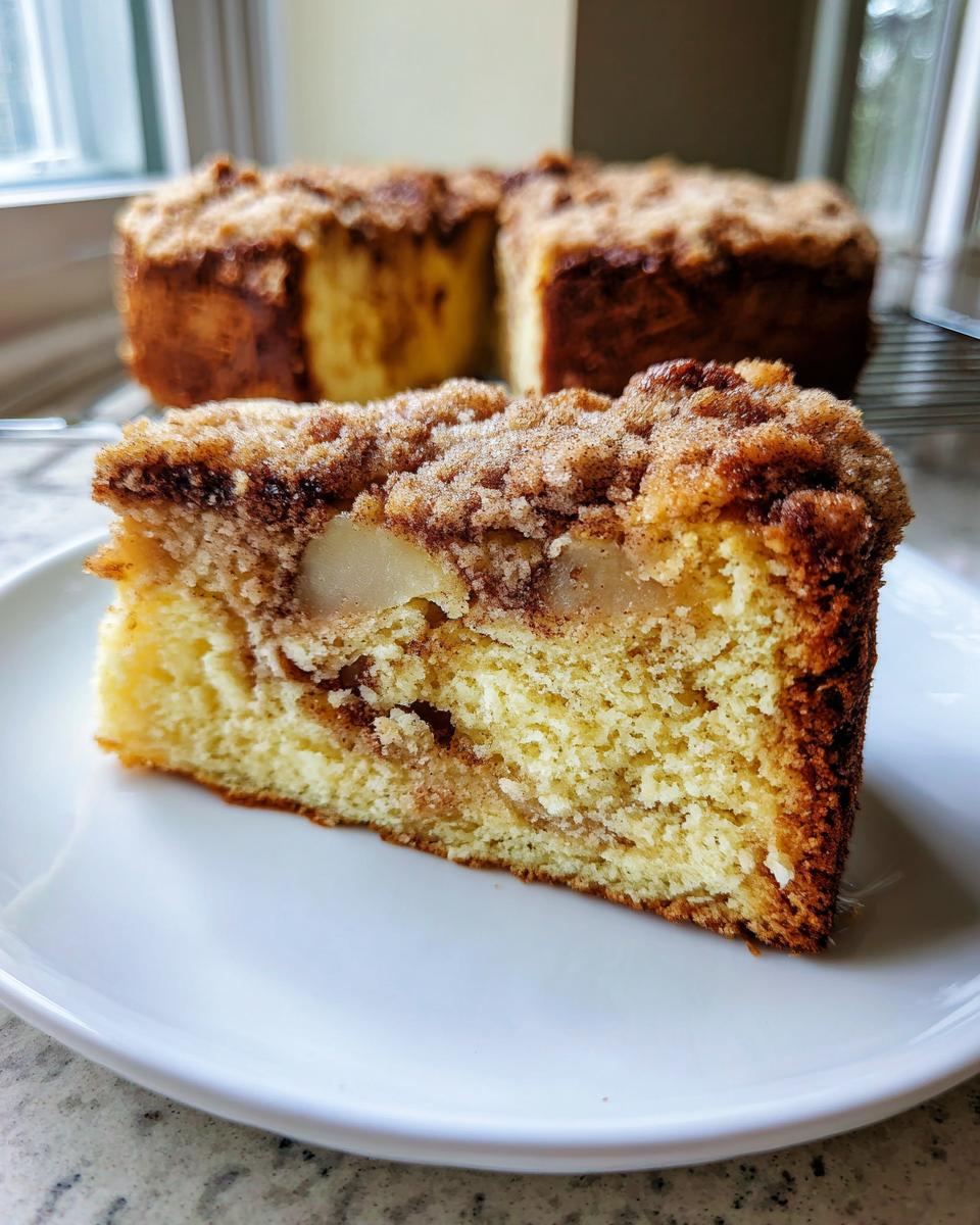 A close-up slice of moist apple crumb cake showing tender cake, apple pieces, and a thick cinnamon crumb topping.