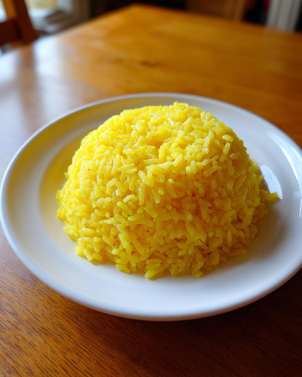A mound of bright yellow turmeric rice served on a white plate atop a wooden table.