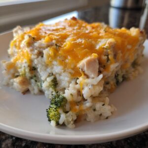 A close-up slice of creamy chicken and broccoli rice casserole topped with melted cheddar cheese.