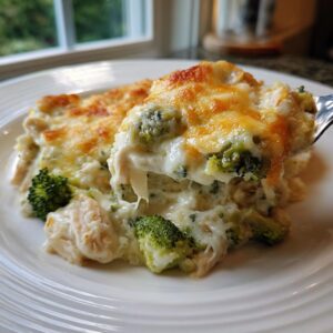 A spoonful of creamy Chicken Divan casserole, featuring melted cheese, chicken, and broccoli florets, being lifted from a white plate.