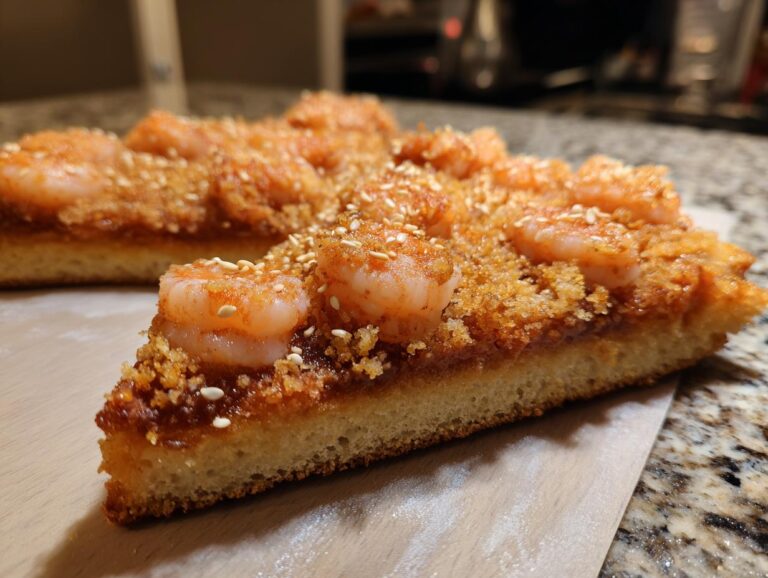 A close-up cross-section view of a thick slice of shrimp toast topped with seasoned shrimp and sesame seeds.