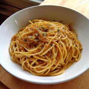 A close-up of creamy caramelized onion pasta served in a white bowl, topped with extra onions and thyme.