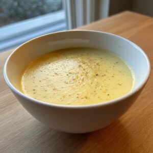 A close-up of a bowl of creamy, yellow cauliflower soup garnished with freshly ground black pepper.