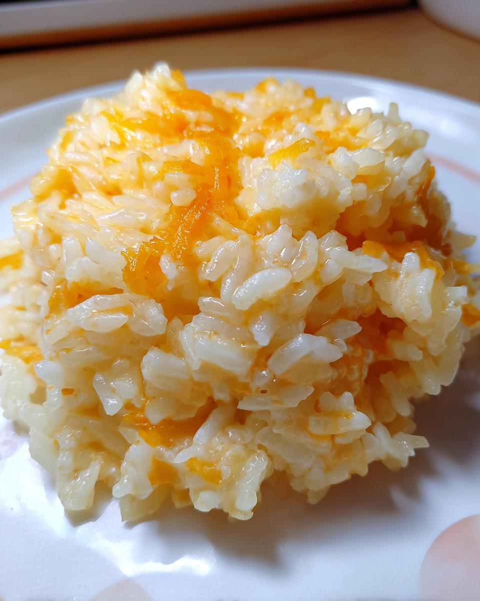 A close-up shot of a mound of creamy, white rice mixed with melted orange cheddar cheese, representing cheesy rice.