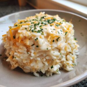 A close-up of a serving of creamy cheesy rice mixed with melted cheese and topped with shredded cheddar and fresh parsley.