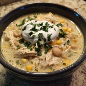 A close-up of a bowl of creamy white chicken chili recipe, topped with sour cream and fresh cilantro.
