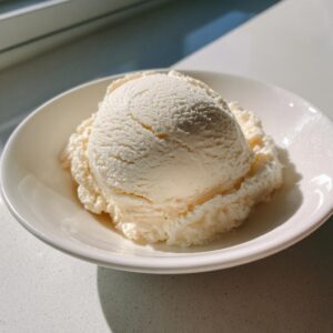 A perfectly scooped serving of creamy, vanilla-colored cottage cheese ice cream in a white bowl.