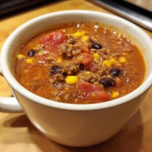 Close-up of a white mug filled with rich, savory cowboy soup containing ground beef, corn, black beans, and tomatoes.