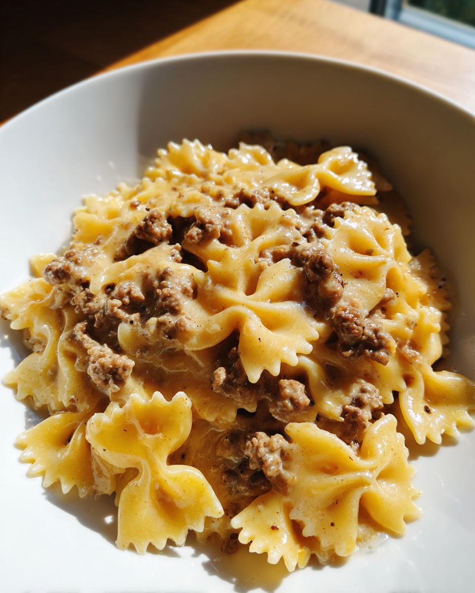 Close-up of creamy parmesan garlic beef bowtie pasta served in a white bowl, richly coated in sauce.