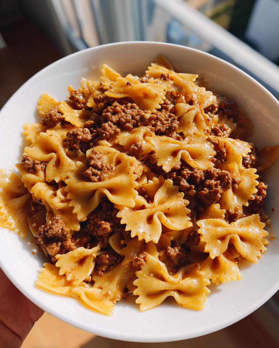Close-up of a white bowl filled with creamy parmesan garlic beef bowtie pasta, featuring bowtie noodles coated in sauce and topped with ground beef.