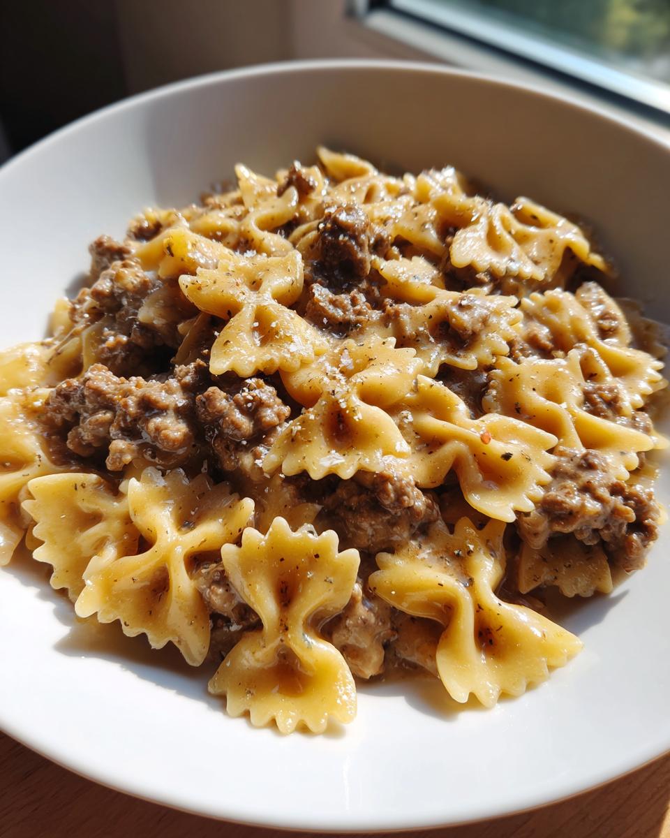 Close-up of creamy parmesan garlic beef bowtie pasta served in a white bowl, seasoned with pepper.