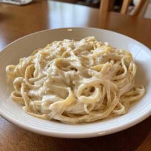 A close-up of fettuccine pasta generously coated in creamy vegan alfredo sauce, served in a white bowl.