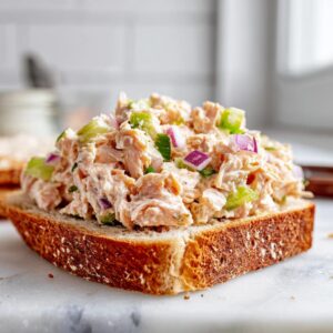 Close-up of creamy salmon salad with celery and red onion served open-faced on a slice of toasted whole-grain bread.