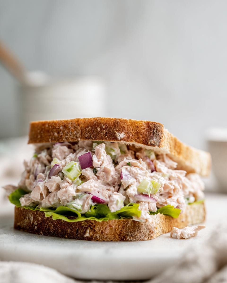 A close-up of a thick sandwich filled with creamy salmon salad, red onion, and celery on toasted bread.