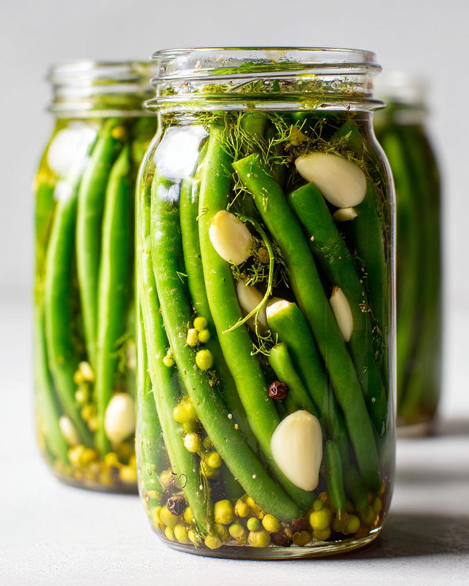 Close-up of fresh green beans packed tightly in a jar with garlic cloves, dill, and peppercorns for making dilly beans.