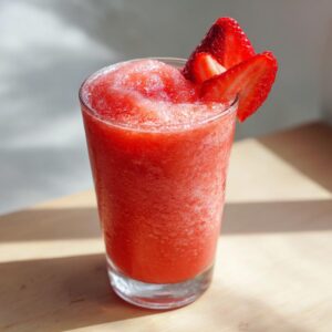 A tall glass filled with a bright red, frozen strawberry daiquiri, garnished with fresh strawberry slices.