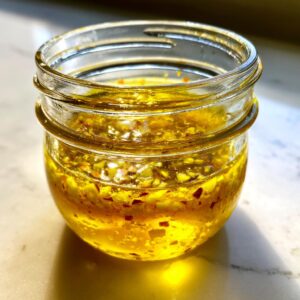 Close-up of homemade golden vinaigrette salad dressing with visible herbs and spices in a small glass jar.