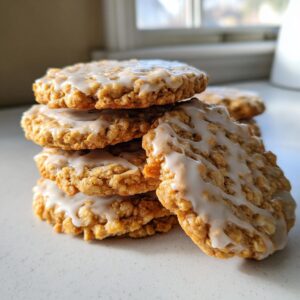 A close-up stack of delicious iced oatmeal cookies drizzled with a thick white glaze, set against a bright background.