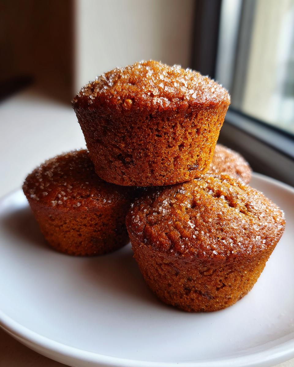 A stack of three moist bran muffins topped with coarse sugar crystals, resting on a white plate.