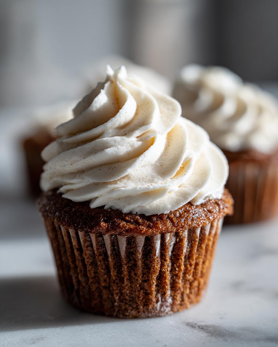 Close-up of a moist gingerbread cupcakes topped with a swirl of vanilla or cream cheese frosting speckled with spices.
