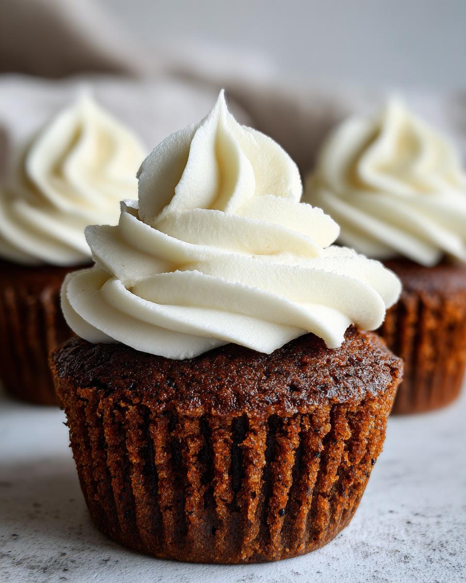 Close-up of a moist gingerbread cupcake topped with a tall swirl of white cream cheese frosting.