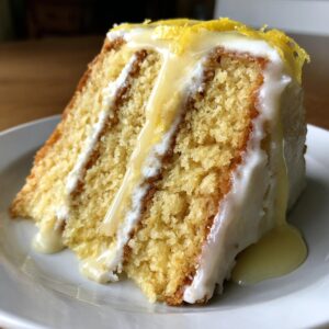 Close-up of a moist slice of lemon cake recipe layered with frosting and drizzled with a thick lemon glaze.