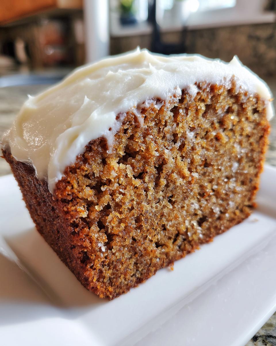 Close-up of a moist slice of spice cake topped with thick white cream cheese frosting on a white plate.