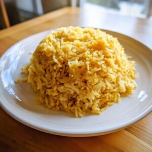 A mound of bright yellow, fluffy turmeric rice served on a white plate.