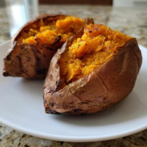 Two perfectly baked sweet potatoes split open, showing fluffy orange flesh seasoned with pepper.