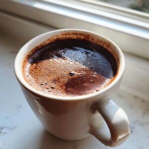 Close-up of a steaming mug filled with rich, dark french hot chocolate, sitting by a window.