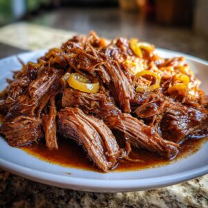 Close-up of juicy, shredded Mississippi Pot Roast served on a white plate with rich gravy and pepperoncini rings.