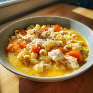 Close-up of a creamy bowl of Sicilian chicken soup featuring shredded chicken, ditalini pasta, carrots, and grated cheese.