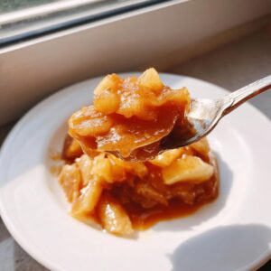 A spoonful of rich, spiced apple pie filling being lifted above a small serving on a white plate.