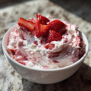 A white bowl filled with fluffy strawberry cheesecake dip, topped with sliced fresh strawberries.