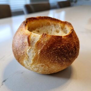 A single, perfectly baked, hollowed-out bread bowl with a golden-brown crust, sitting on a light countertop.