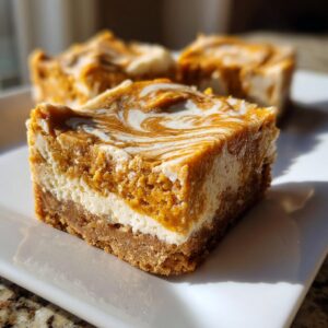 A close-up of a decadent, layered pumpkin cheesecake bars square with a beautiful orange and white swirl topping.