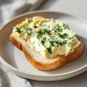 A thick slice of toasted bread generously spread with creamy garlic butter and topped with fresh chopped parsley.