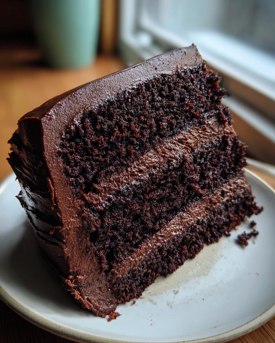 Close-up of a moist slice of ultimate chocolate fudge cake layered with thick, dark chocolate frosting.