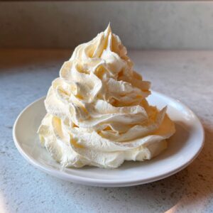 A tall, perfectly piped swirl of light yellow vanilla buttercream frosting sitting on a small white plate.
