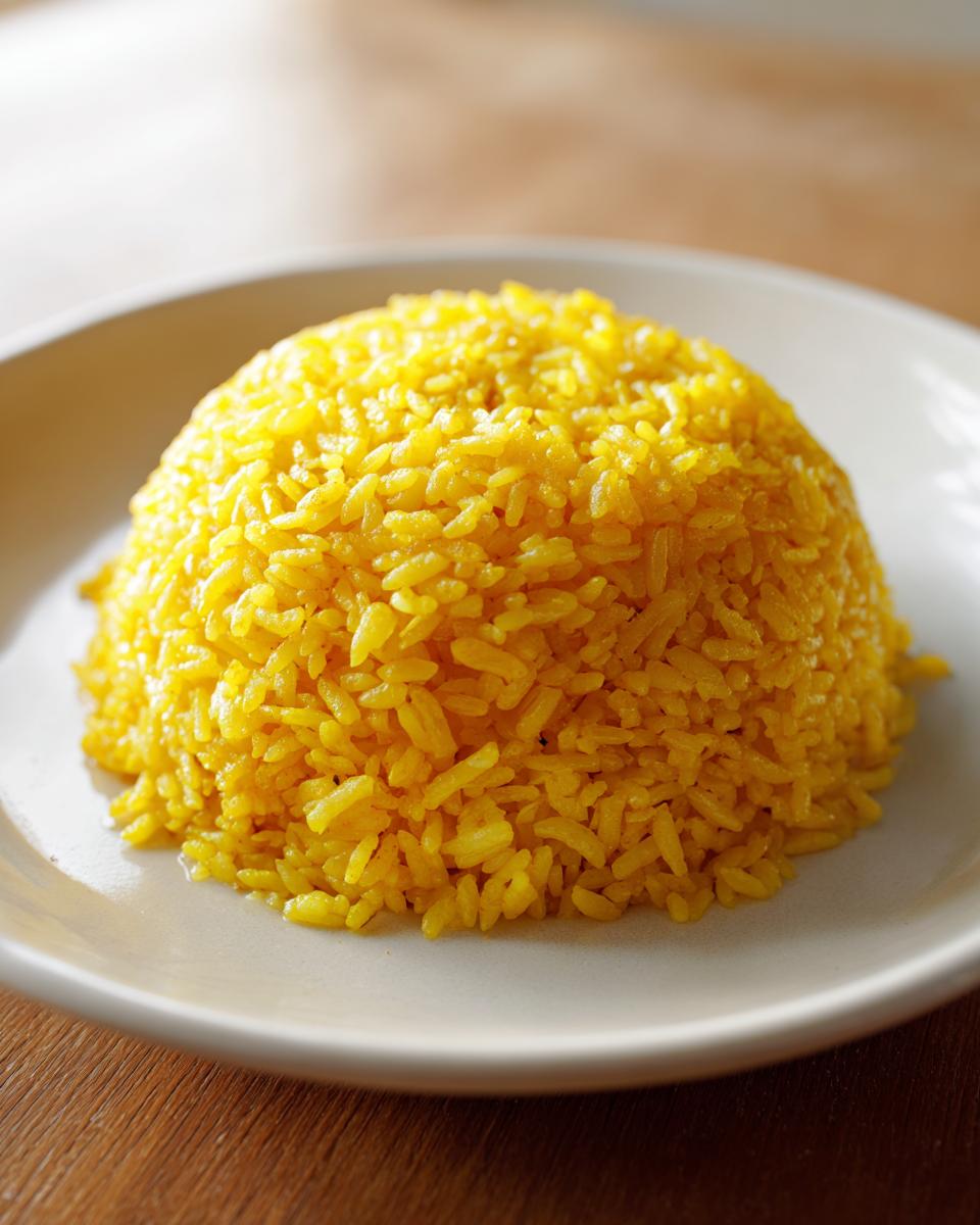 A dome-shaped serving of vibrant yellow turmeric rice presented on a light-colored plate.