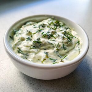 Close-up of creamy homemade tartar sauce topped generously with fresh dill in a small white bowl.