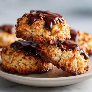 A stack of golden brown, chewy almond joy cookies drizzled generously with melted dark chocolate.