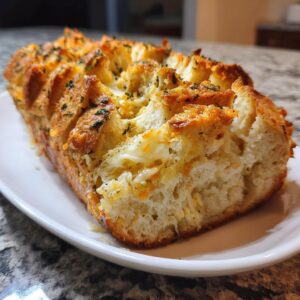 A golden-brown loaf of pull-apart cheese bread, oozing with melted cheese and topped with herbs.