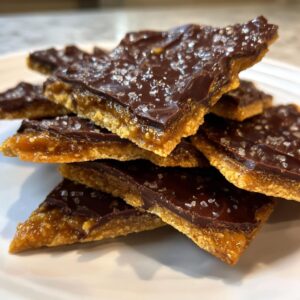 A stack of homemade graham cracker toffee pieces topped with melted dark chocolate and flaky sea salt.
