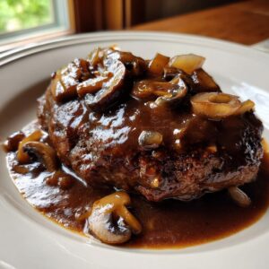 A juicy salisbury steak smothered in rich brown mushroom gravy and sautéed onions, served on a white plate.